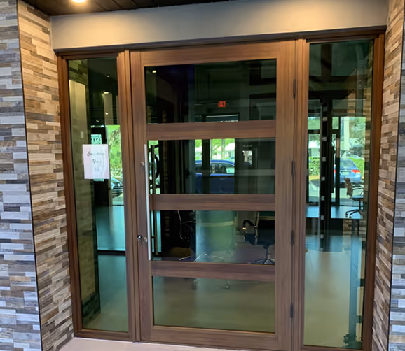 Modern commercial doors with large glass panels and sidelights, set in a stone-textured wall entrance.