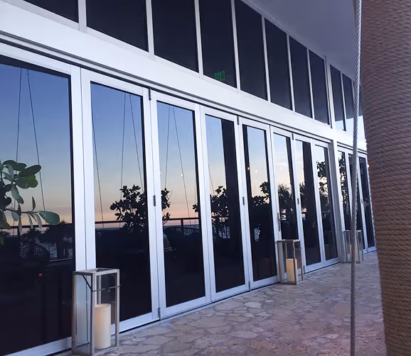 Glass doors reflecting sunset sky and plants, with candles in glass lanterns on stone floor.