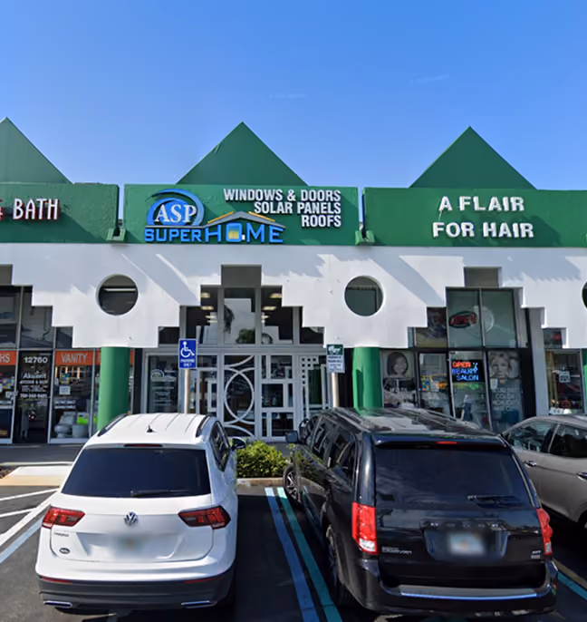 Storefront with green peaked roof featuring signs for ASP Super Home Windows & Doors Solar Panels Roofs and A Flair For Hair salon, with cars parked in front.
