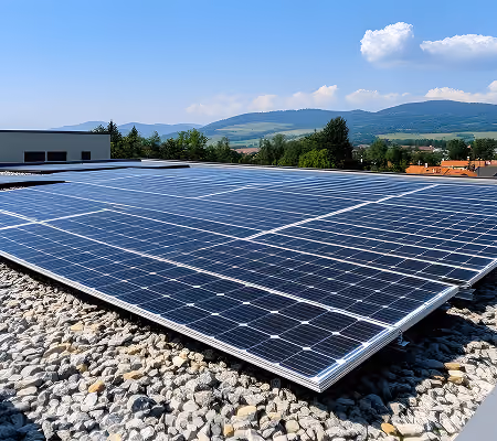 Solar panels installed on a gravel rooftop with mountains and trees in the background under a clear blue sky.