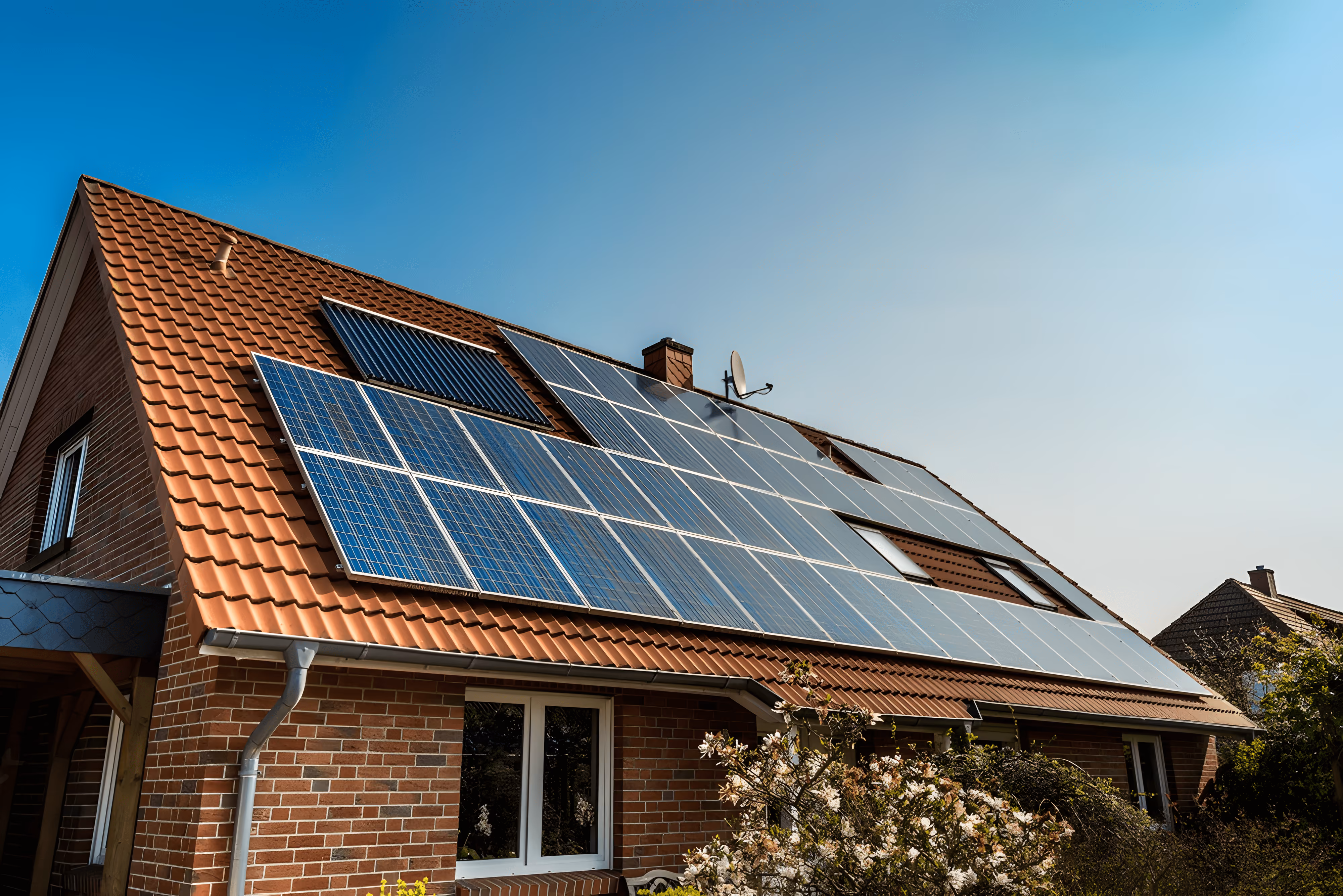 House with a red tiled roof equipped with multiple solar panels under a clear blue sky.