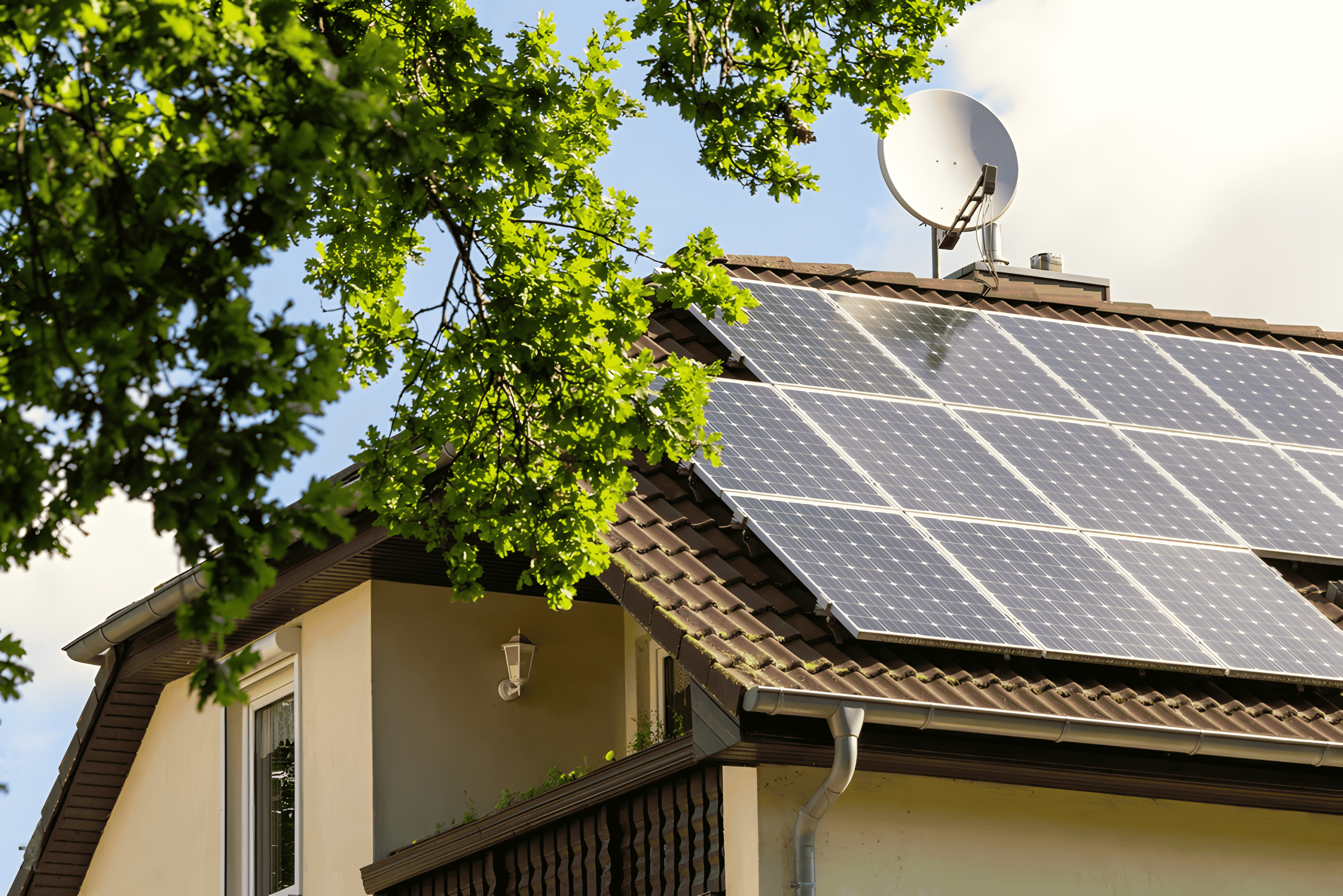 Solar panels installed on the roof of a house with green tree branches in the foreground.