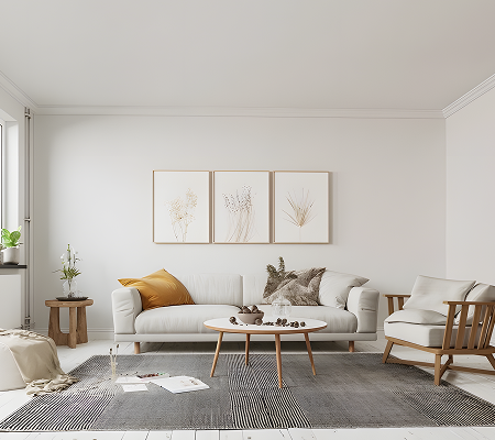 Minimalist living room with a beige sofa, a wooden armchair, a white coffee table, three framed botanical prints, and a black and white rug.