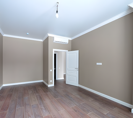 Empty room with beige walls, wooden floor, white door slightly open, and ceiling-mounted air conditioner.