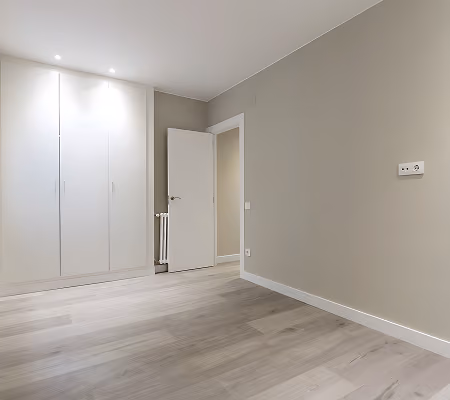 Empty room with light wood flooring, beige walls, white built-in wardrobe, and a partially open door.