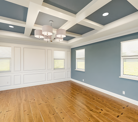 Empty room with wooden floors, white and blue walls, coffered ceiling with light fixture, and two windows with blinds.