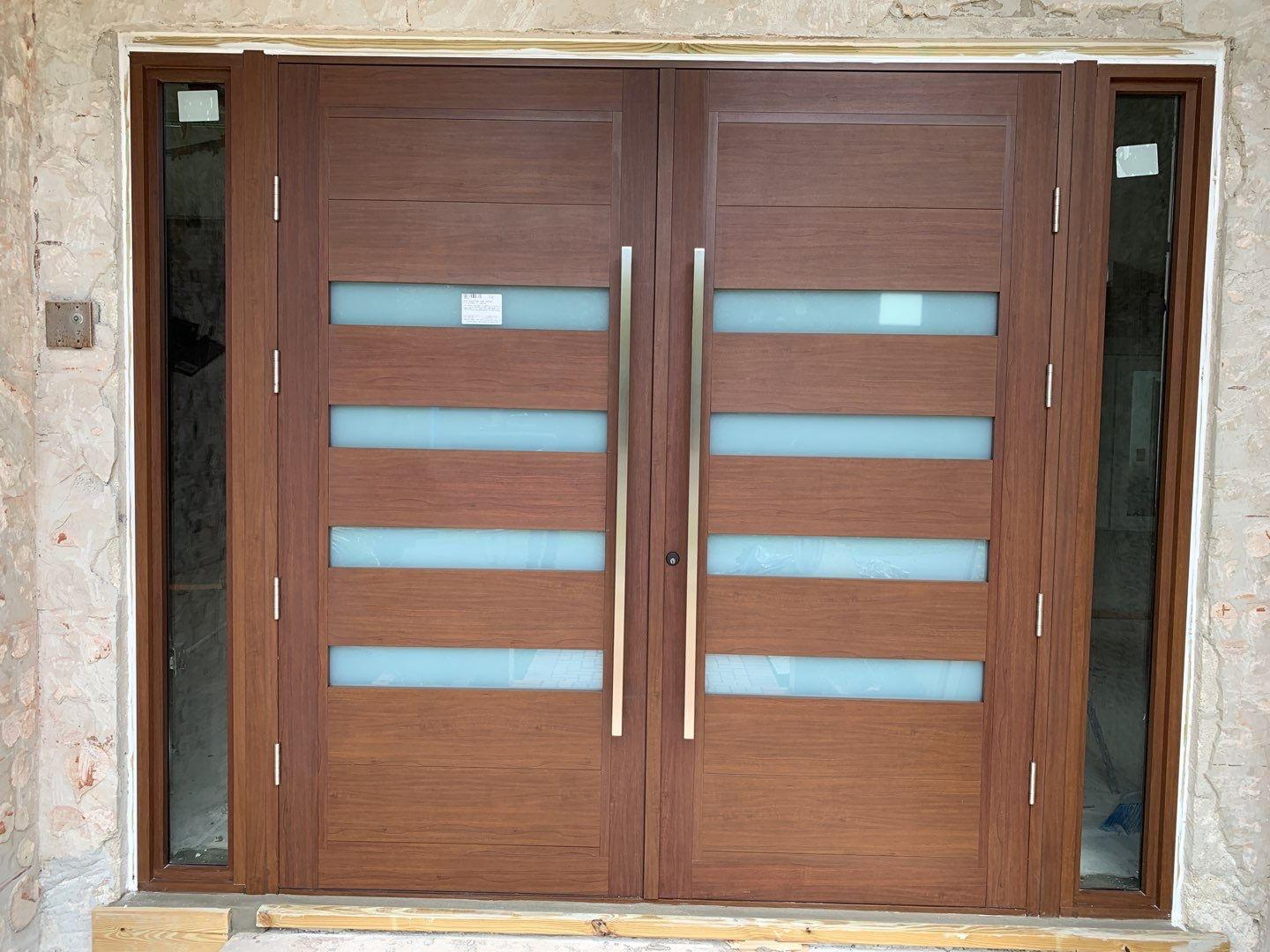 Double wooden front entry doors with horizontal frosted glass panels and metal handles, framed by stone walls.