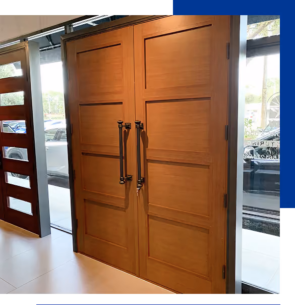 Residential impact doors with vertical panels edark metal handles inside a building near glass windows showing parked cars outside.