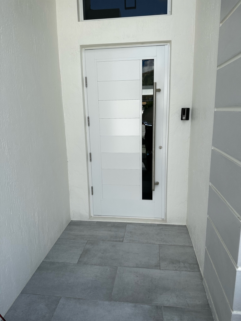 White modern entry door with horizontal panels, a vertical glass window strip, silver handle, and a doorbell on the right wall.