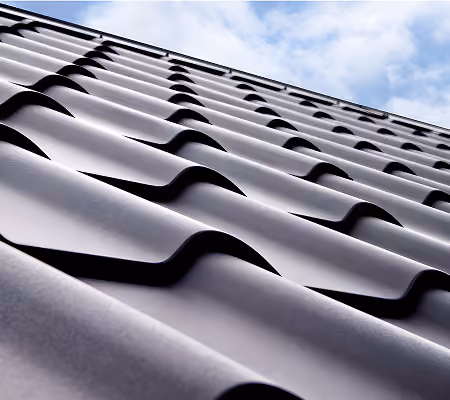 Close-up view of dark metal roofing tiles with a partly cloudy sky in the background.
