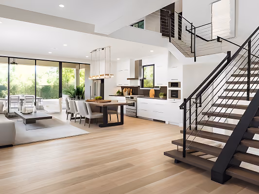 Modern open-concept living space with a kitchen, dining table, living area, and stairway with metal railing.