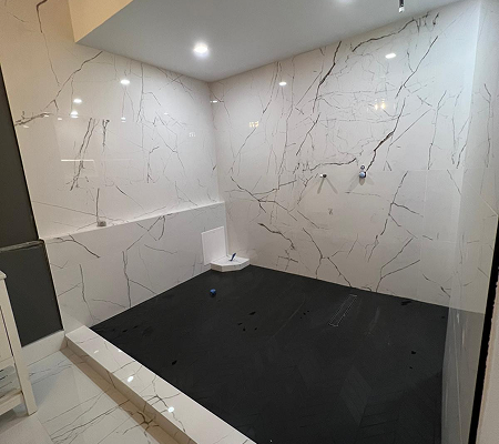 Modern walk-in shower under construction with black floor tiles and large white marble-patterned wall tiles.