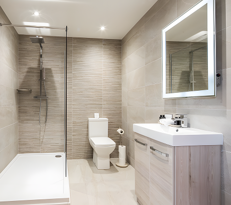 Modern bathroom with walk-in glass shower, white toilet, and light wood vanity with illuminated mirror.