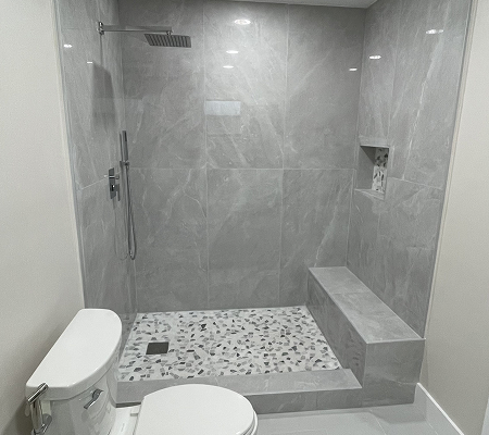 Modern walk-in shower with large gray marble tiles, terrazzo floor, built-in bench, and overhead rain showerhead.