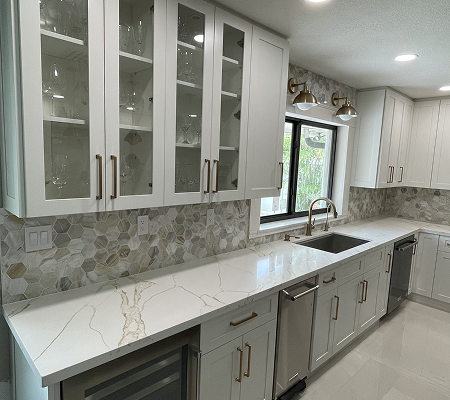 Modern kitchen with white cabinets, marble countertop, glass-front upper cabinets, stainless steel appliances, and hexagonal tile backsplash.