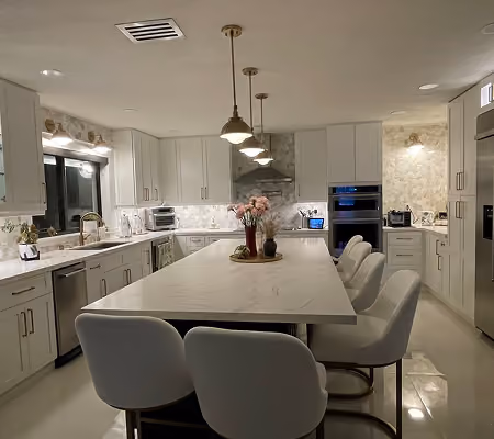 Modern kitchen with white cabinets, marble island, six chairs, pendant lights, and stainless steel appliances.