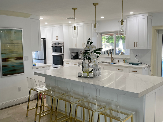 Modern kitchen with white cabinets, marble countertop island with transparent bar stools, and pendant lights overhead.