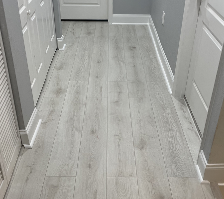 Hallway with light gray wood laminate flooring, surrounded by white doors and gray walls.