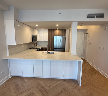 Modern kitchen with white marble countertop island, built-in microwave, stainless steel refrigerator, and wooden flooring.