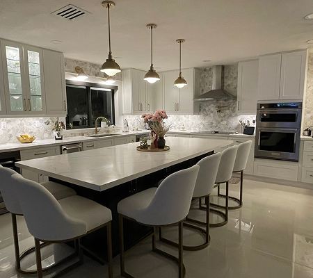 Modern kitchen with white cabinetry, marble countertops, center island with seating, pendant lights, and stainless steel appliances.