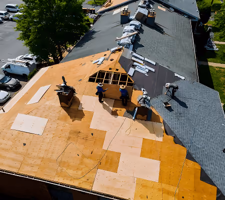 Aerial view of workers installing a wooden roof deck and shingles on a large building under renovation.