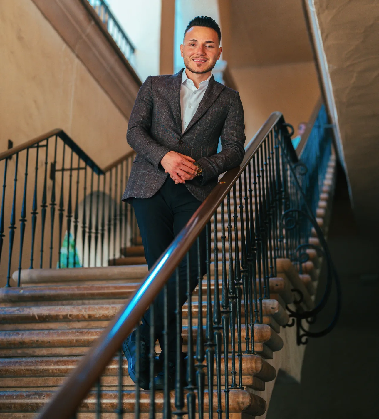 Man in a suit standing on a staircase inside a classic building.