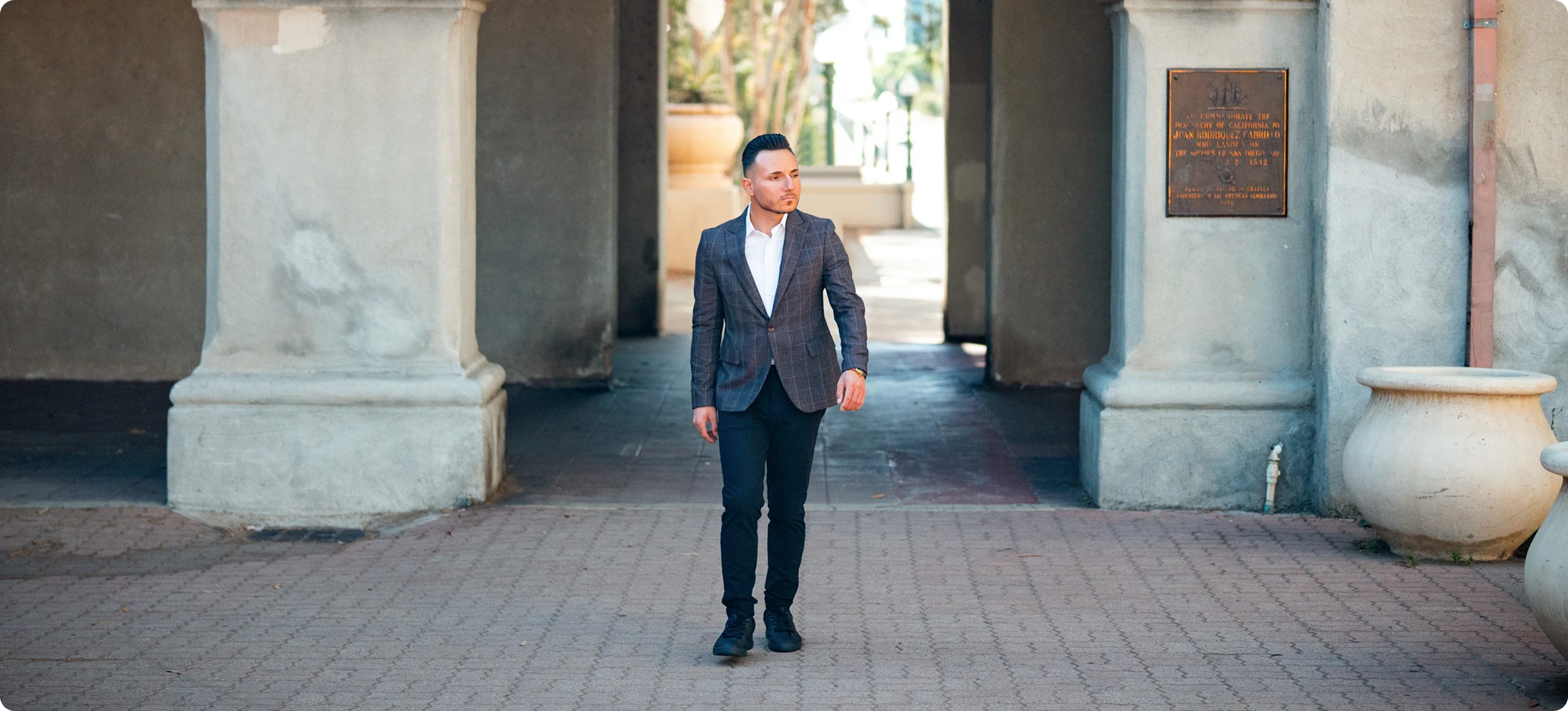 Man in a tailored blazer walking through an arched stone corridor