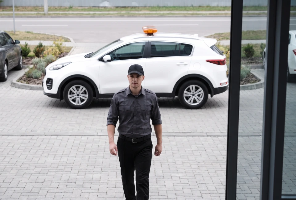 Security responder approaching a building entrance with a marked response vehicle parked behind him.