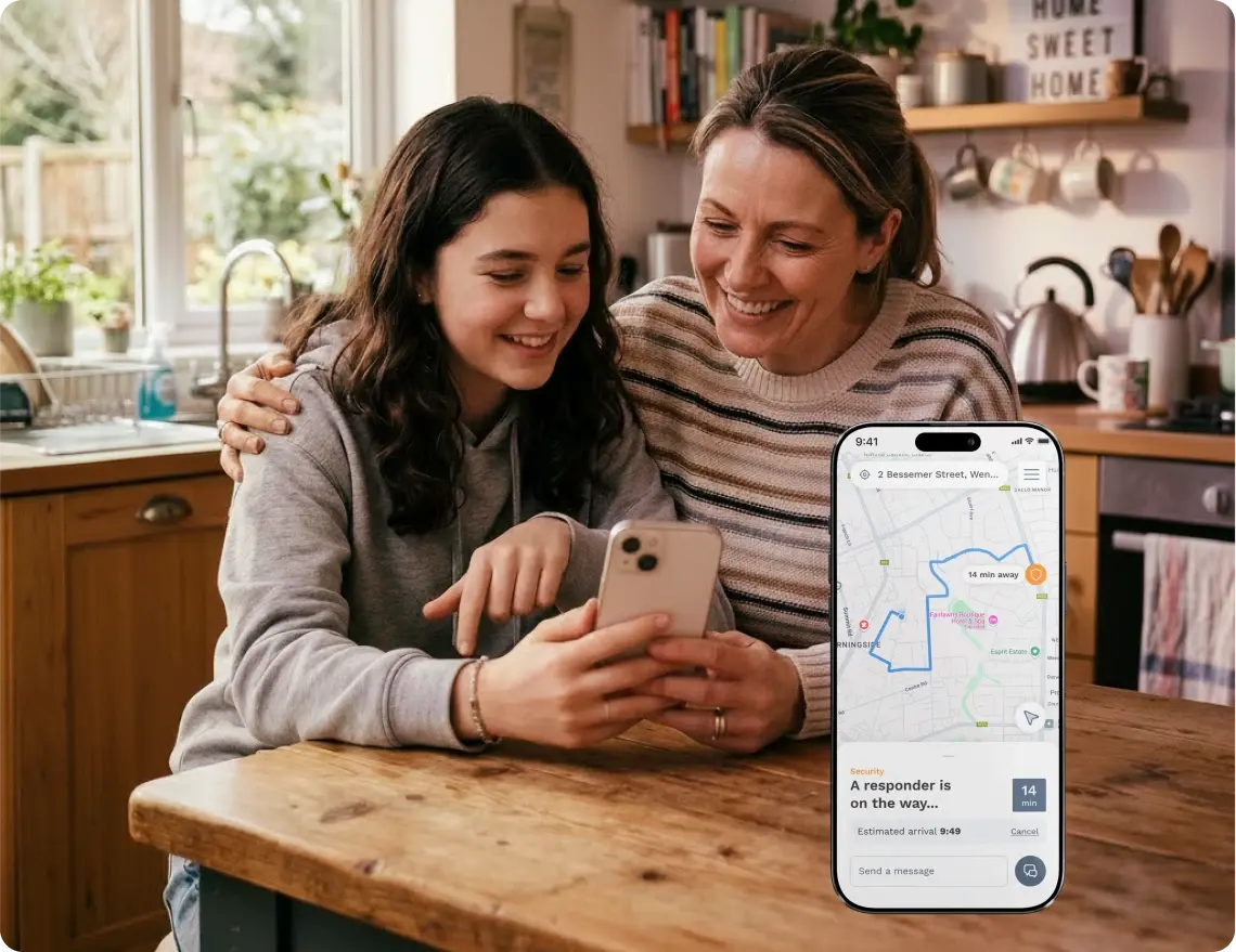 Mother and teenage daughter at a kitchen table looking at a phone showing a security responder 14 minutes away