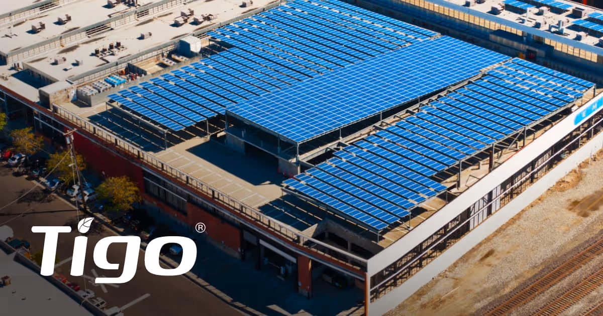 Zdjęcie lotnicze rozległej instalacji fotowoltaicznej na dachu wielopoziomowego parkingu i budynku komercyjnego, z widocznym logo Tigo.