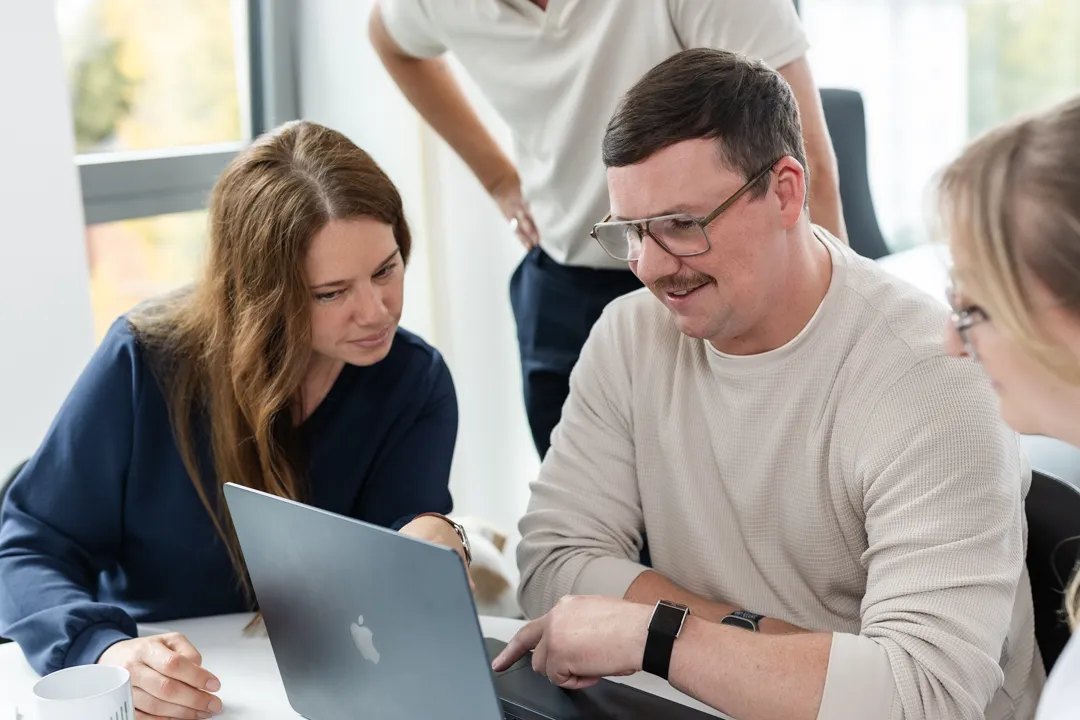 Gruppengespräch von drei Personen, die auf einen Laptop schauen und zusammenarbeiten.