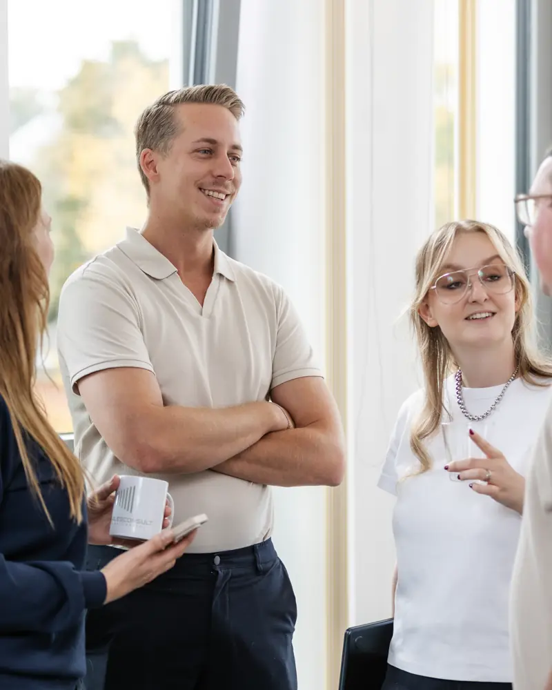 Gruppe von vier jungen Erwachsenen, die freundlich in einem hellen Raum miteinander sprechen.