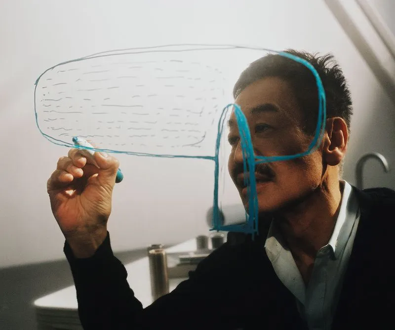 Man drawing a blue schematic design on a transparent surface.