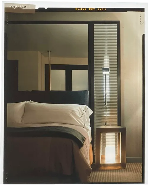 Modern bedroom with a neatly made bed, dark headboard, and a geometric bedside lamp emitting warm light.