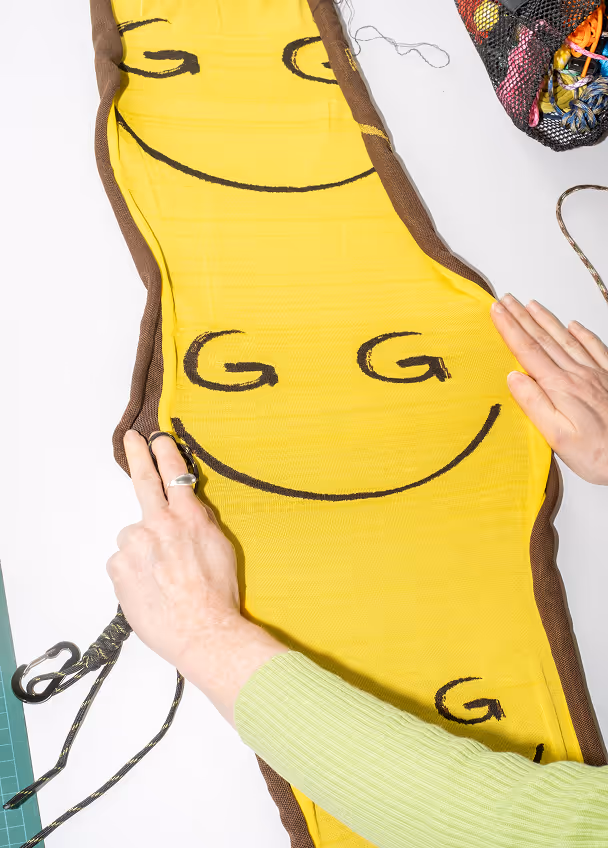 Hands adjusting a yellow fabric panel with black smiley faces outlined by brown trim on a white surface.