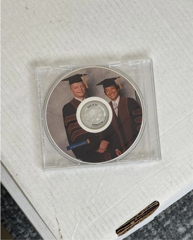 DVD case on cardboard box featuring a photo of two men in graduation caps and gowns shaking hands.