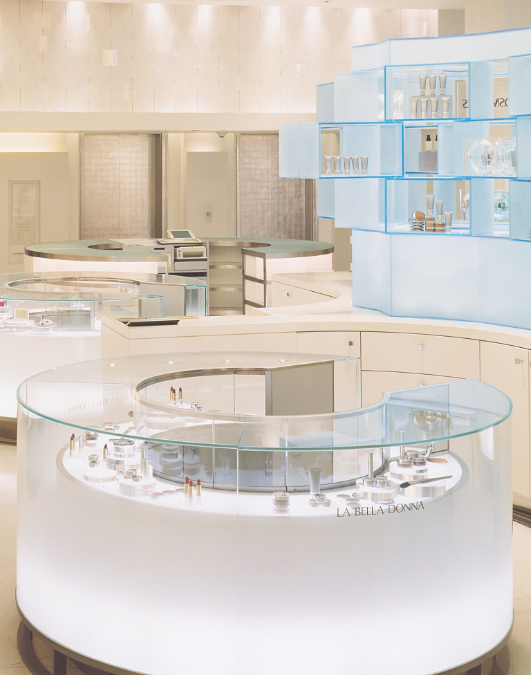 Modern retail display counters with glass tops showcasing beauty products in a bright, minimalist store interior.