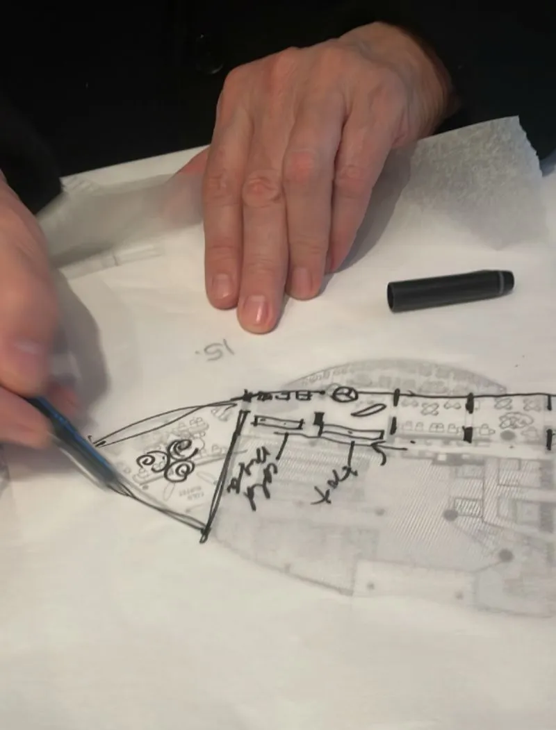 Hands sketching and marking on a transparent architectural floor plan with a pen and marker cap nearby.