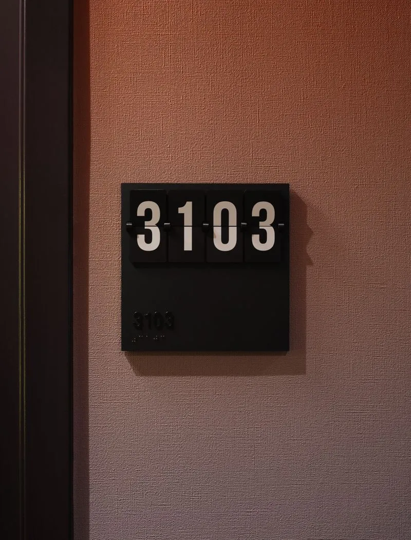 Black room number plaque displaying number 3103 mounted on a textured brown wall.