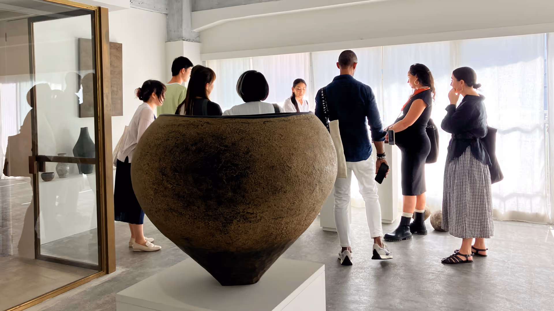 Group of people viewing a large ceramic vase displayed on a pedestal in a bright gallery space.
