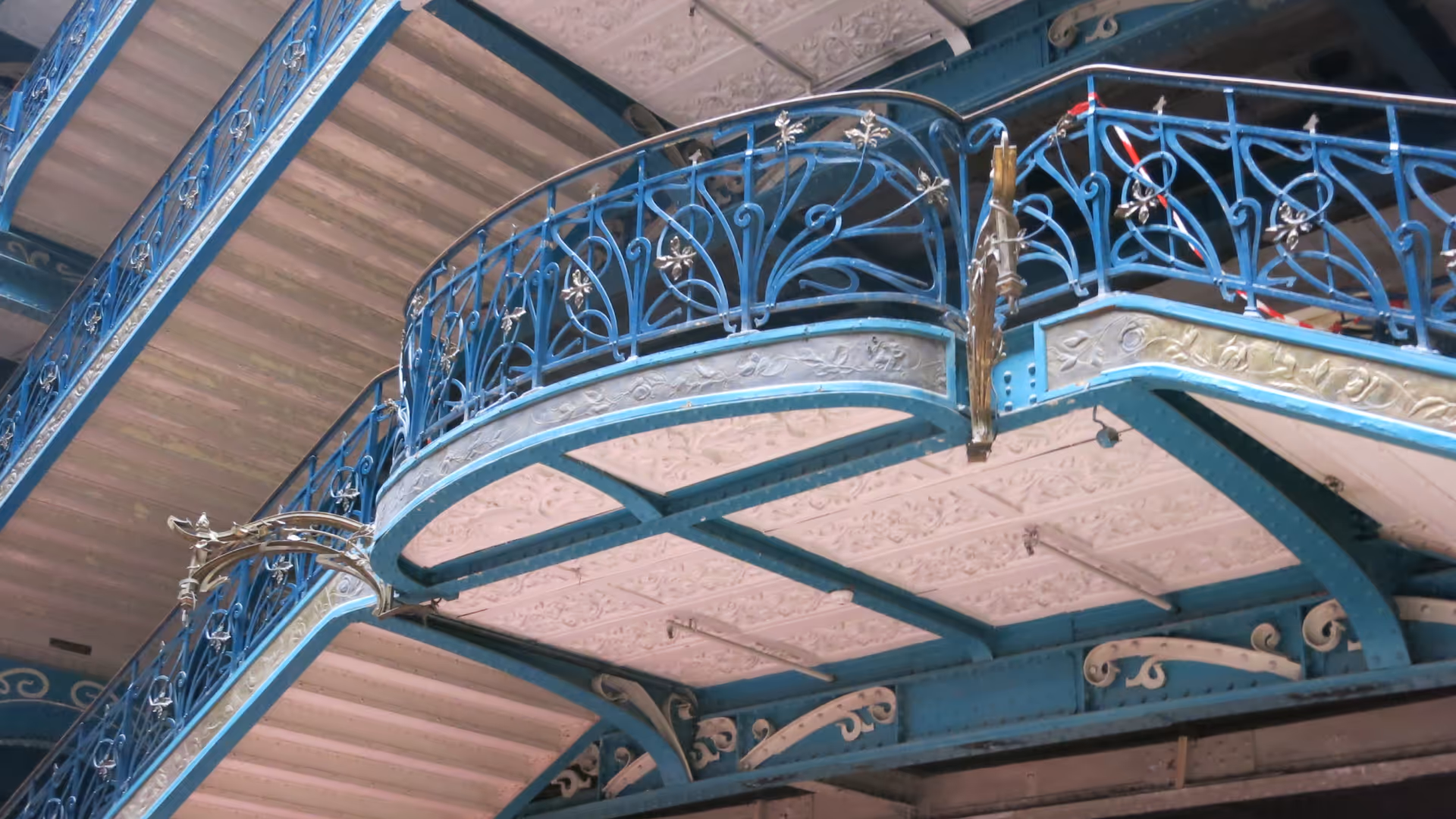 Ornate blue and white metal balcony with decorative railing and floral motifs on ceiling panels.