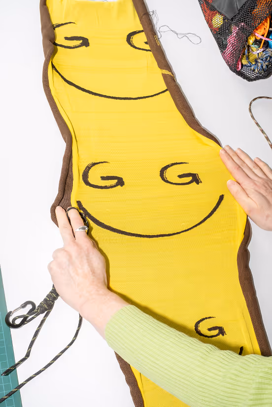 Hands working on a yellow fabric piece with smiley faces and brown edges on a white table.