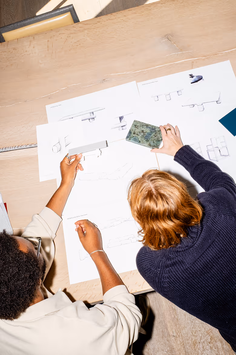 Two people collaborating at a table reviewing design sketches and holding a green stone sample.