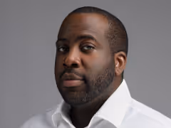 Portrait of a man with short hair and beard wearing a white shirt against a gray background.