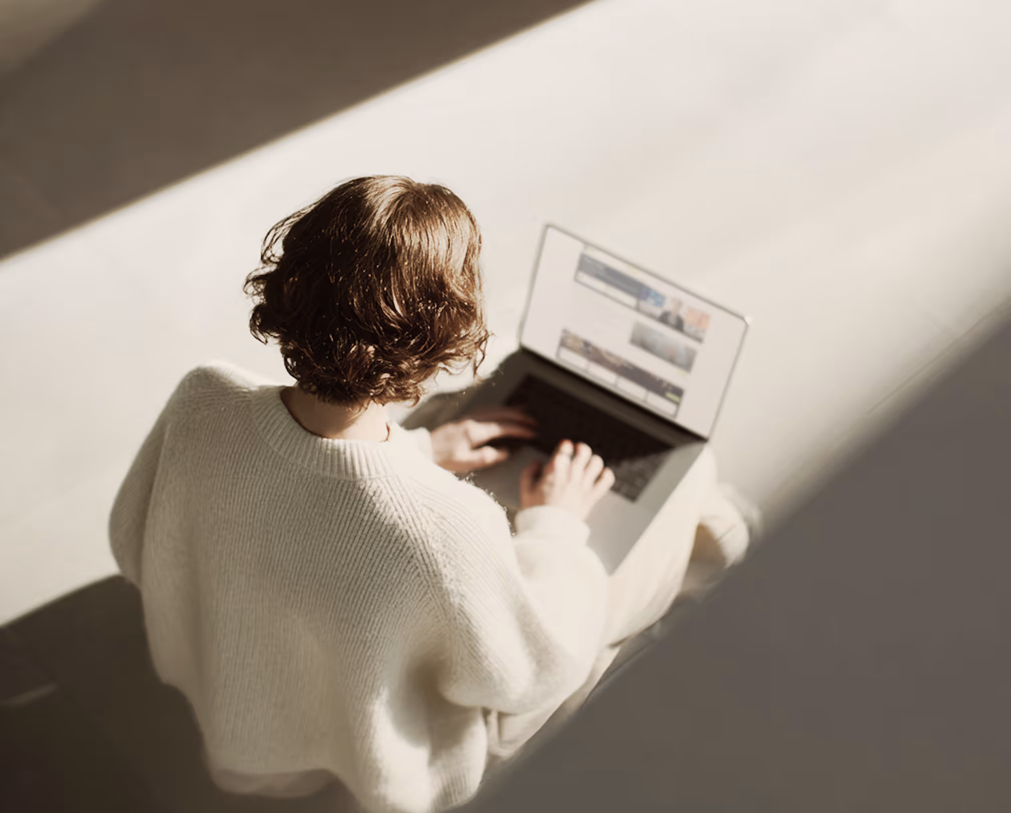 Person mit kurzen braunen Haaren in weißem Pullover tippt auf einem Laptop mit OpenAI-Logo, sitzend in hellem Raum.