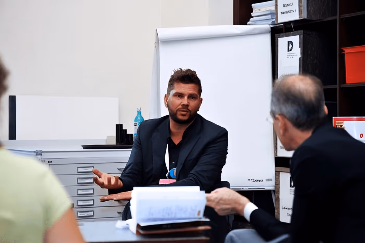 Man in dark blazer presenting documents during office meeting with colleagues