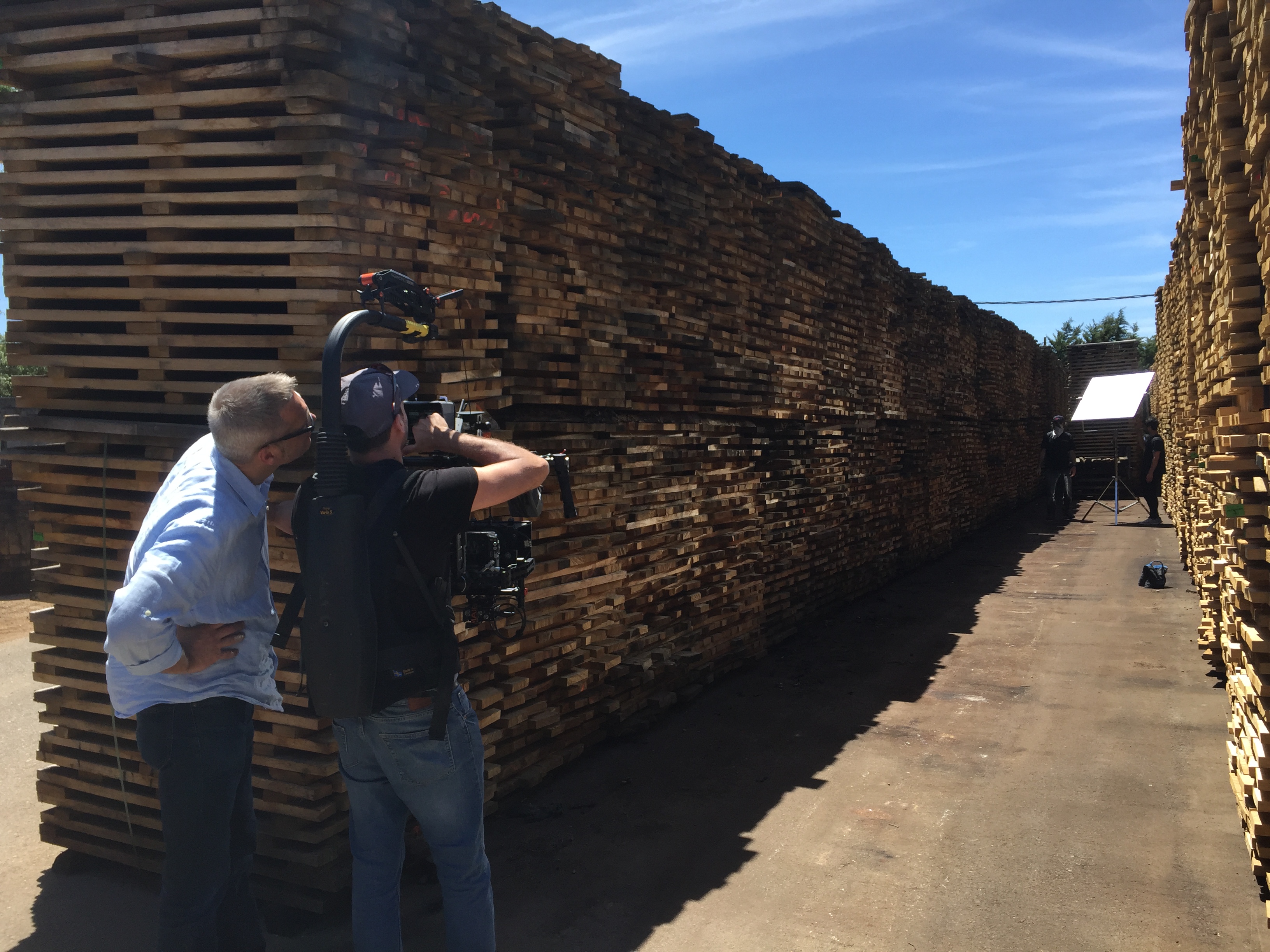Cameraman and director filming between stacked wooden pallets on sunny day