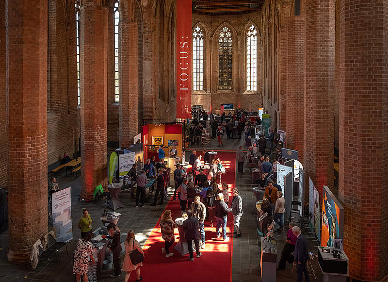 Crowded event inside historic brick church with vaulted Gothic windows and red carpet.
