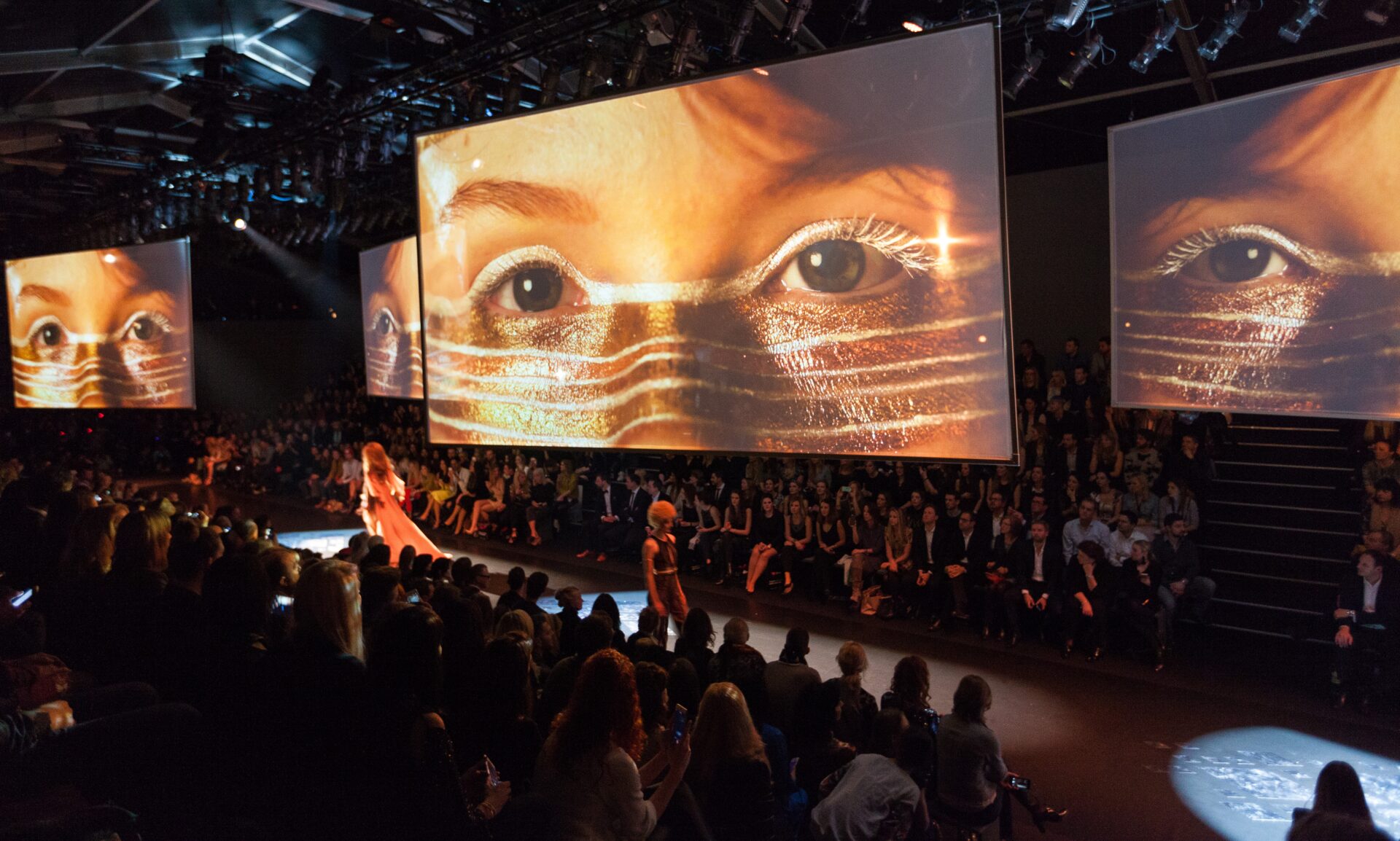 Large concert venue displays close-up of golden eyes on massive screens above crowd