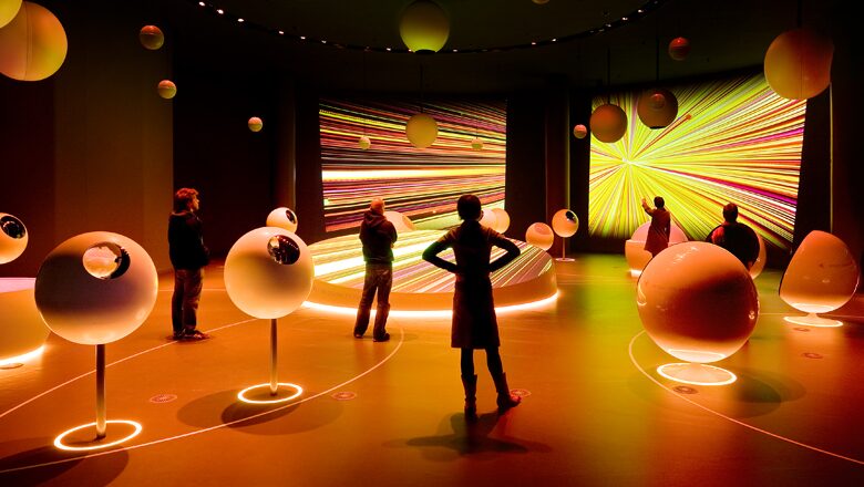 Interactive art installation with glowing orange spheres and colorful light projections on walls